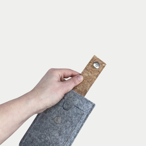 Hand, die eine graue Motorola Edge-Hülle aus Filz mit Korkdetails und Magnetverschluss für das Motorola Moto G75 hält.