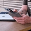 Handytasche für Google Pixel 10 aus grauem Wollfilz, gehalten von einer Person, mit Laptop im Hintergrund.