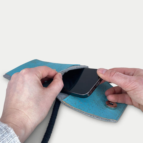 Person, die ein Motorola Moto G85 in eine stilvolle hellgraue und blaue Filztasche mit Schulterriemen steckt.